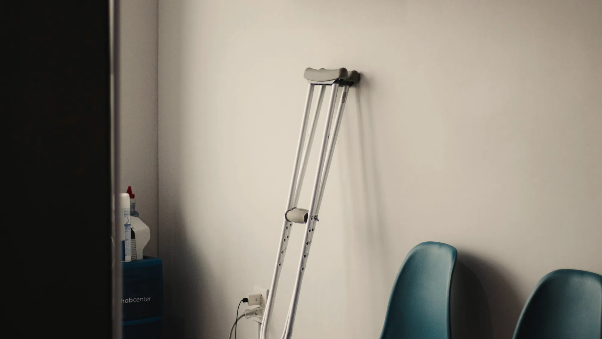 A pair of crutches resting against a pale wall beside empty waiting-room chairs