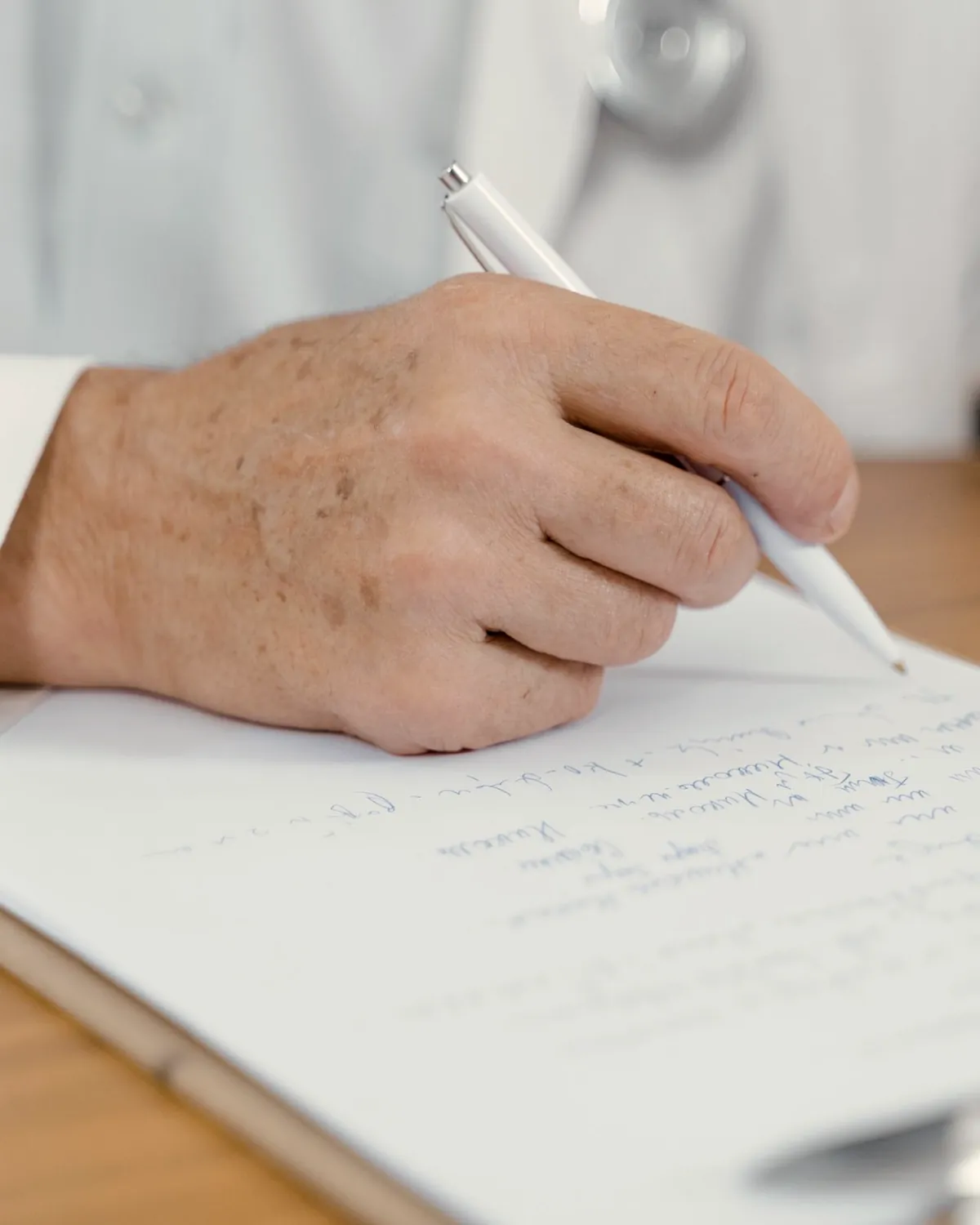 Close-up of a hand writing notes on a clipboard at a wooden desk